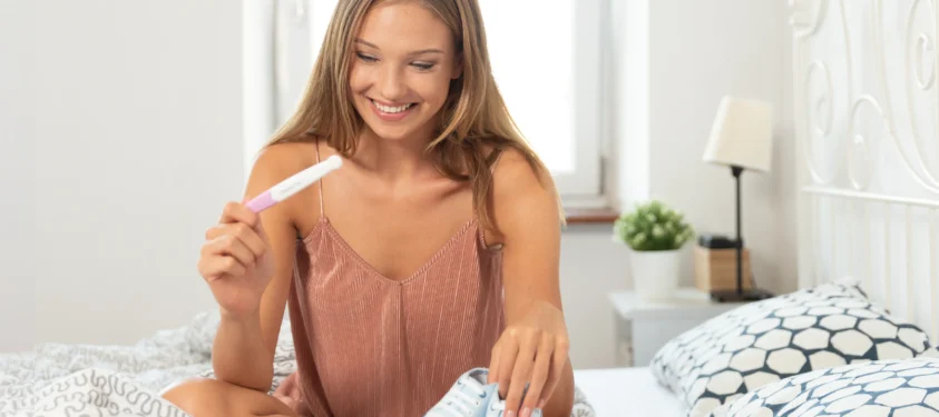 Woman on bed holding pregnancy test